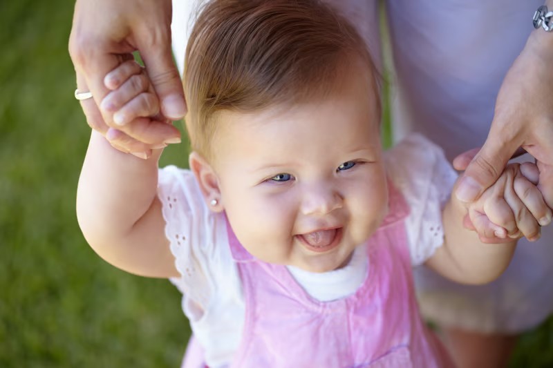 A caregiver helping a baby take early steps outdoors