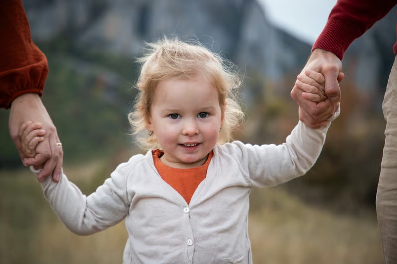 A young child smiling while holding hands with caregivers in a field