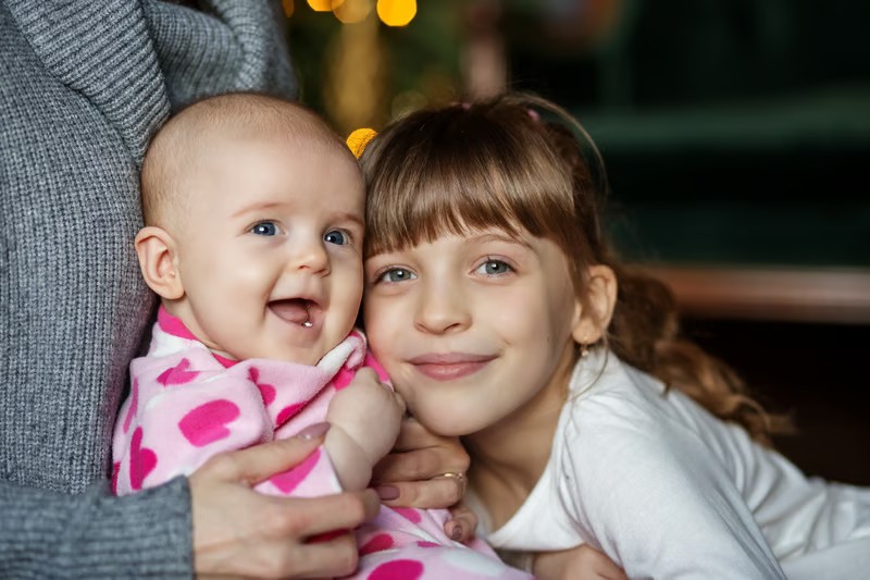Two young siblings smiling while held close by a caregiver